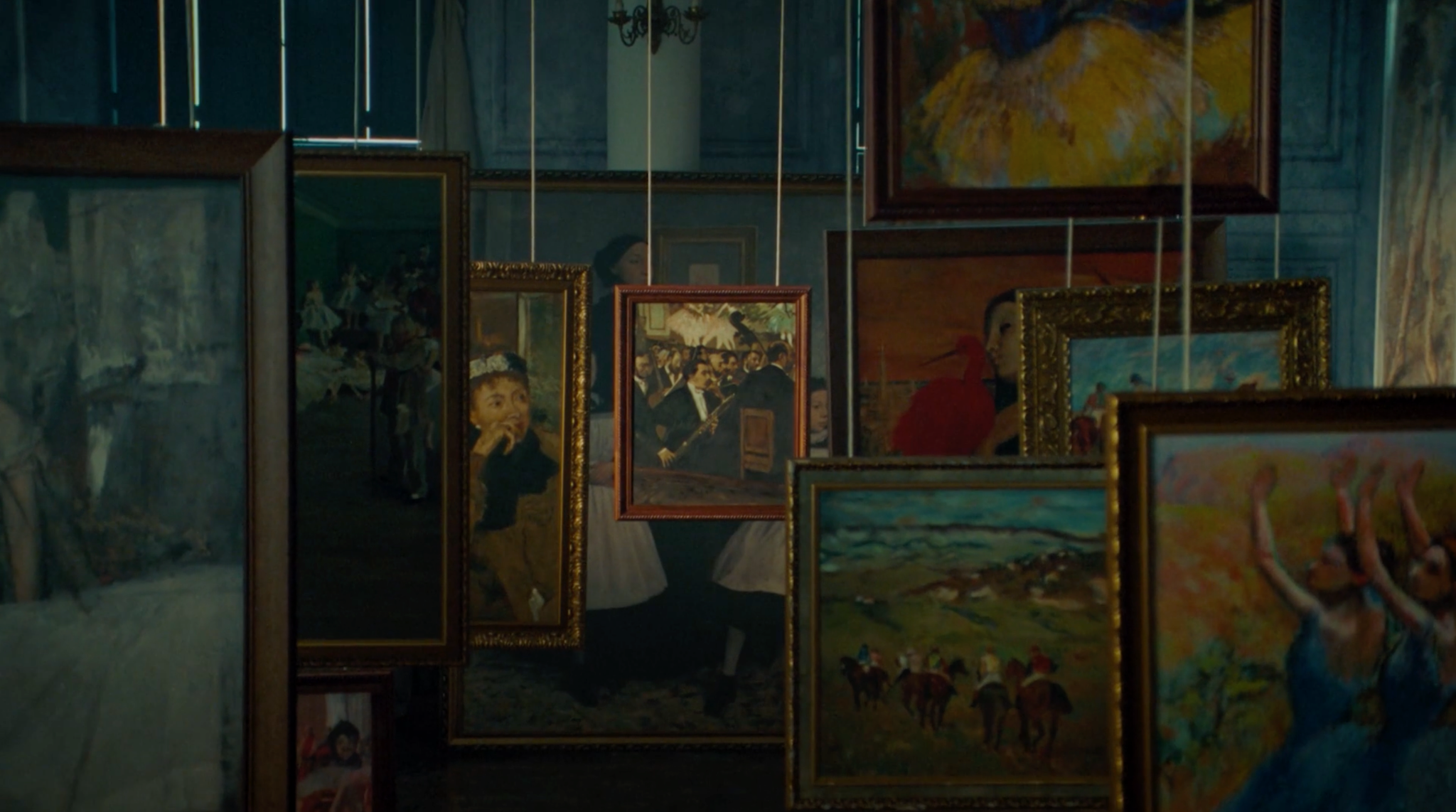 Pinturas emolduradas e cavaletes organizados diante de uma parede azul.