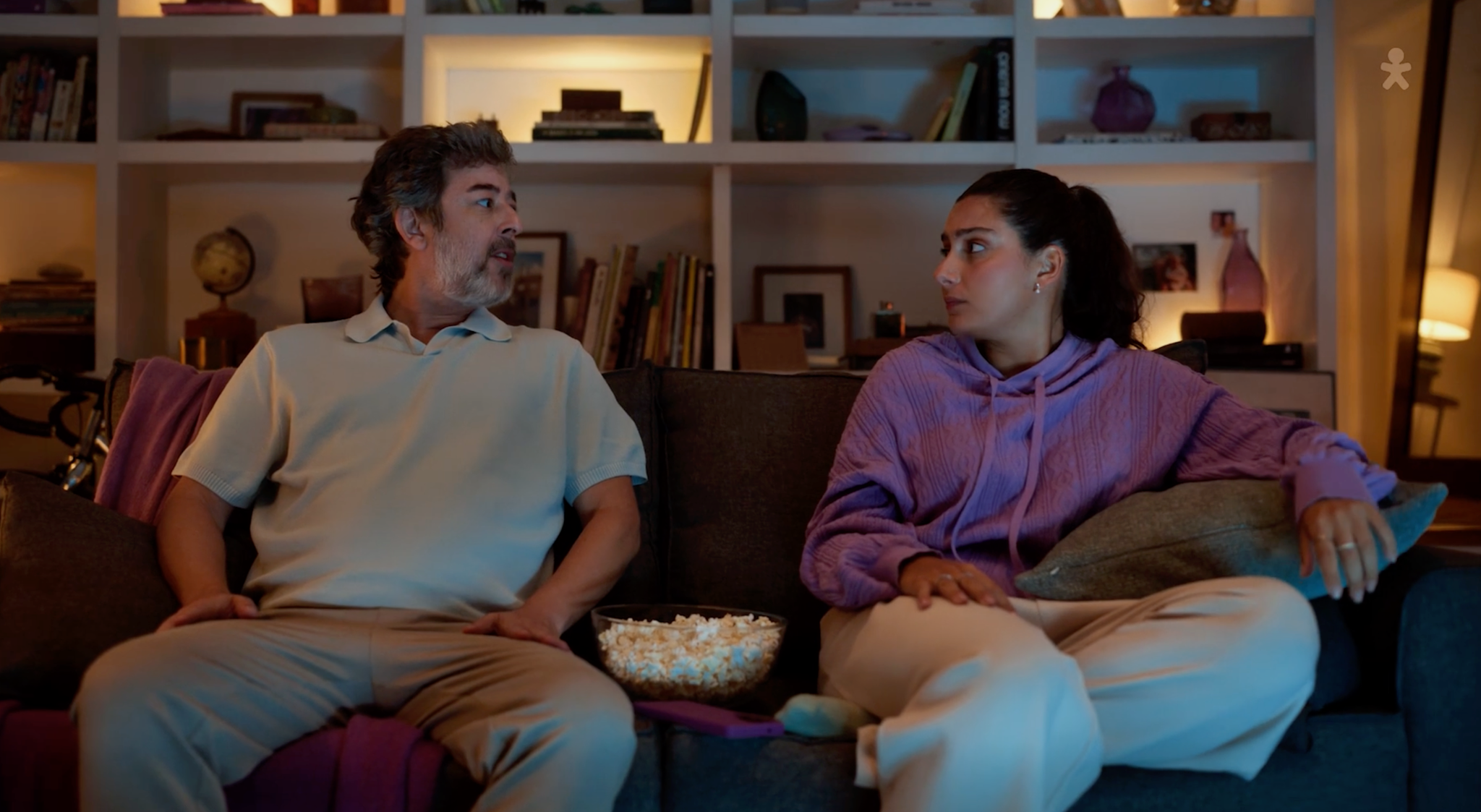 Casal conversando no sofá com uma tigela de pipoca entre eles.