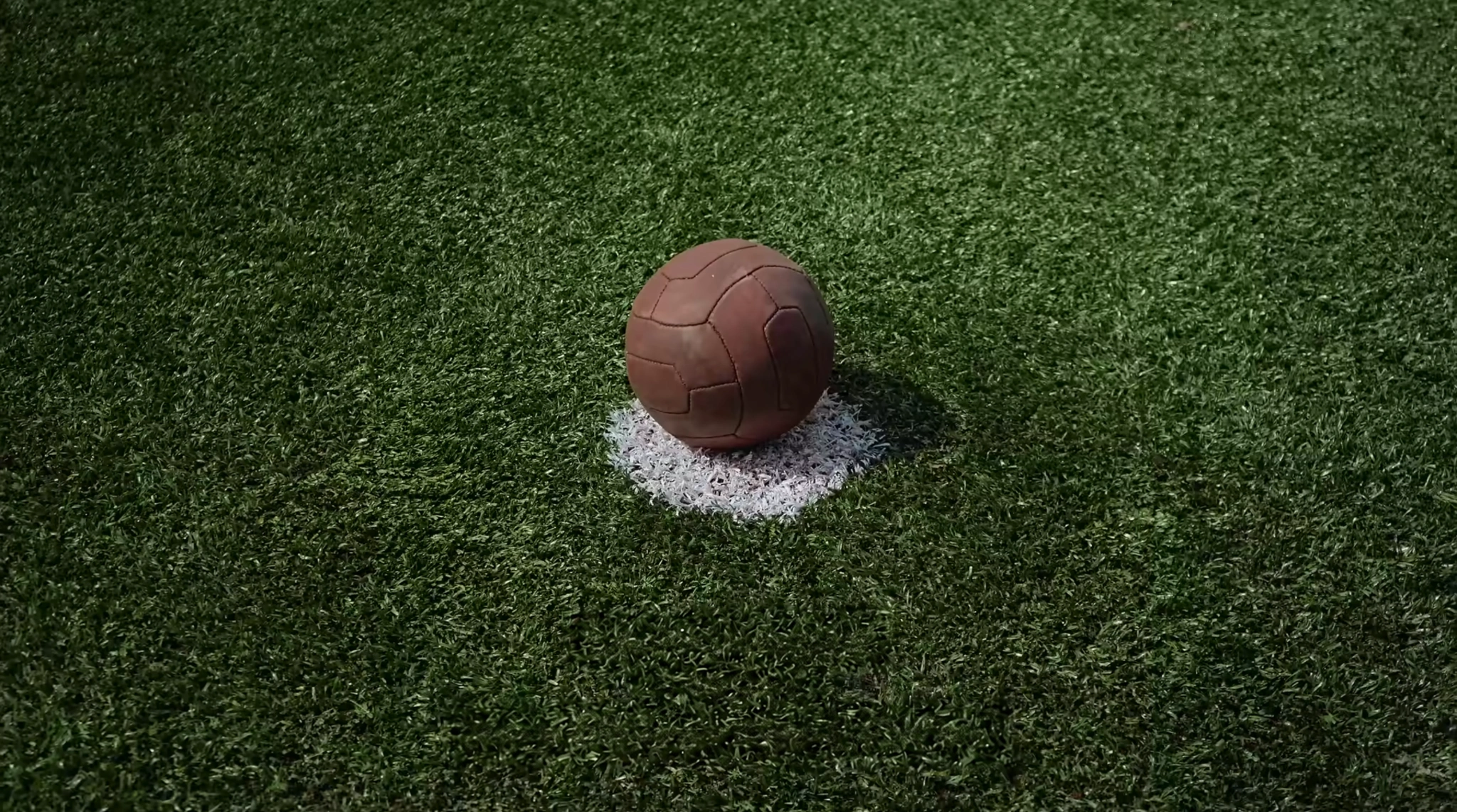Bola de couro sobre uma marca branca no gramado.