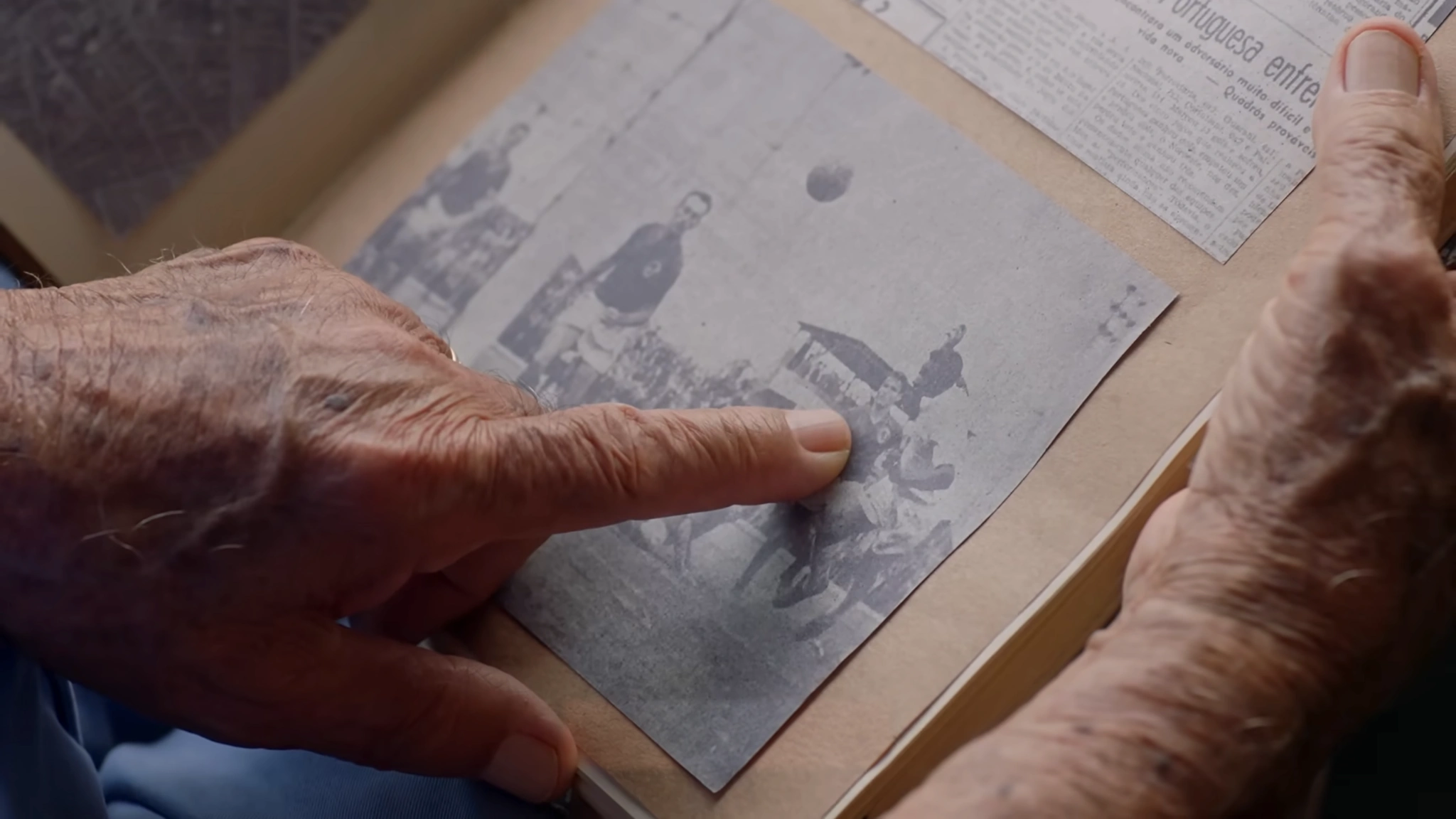 Mãos folheando um álbum de fotografias antigas de futebol.