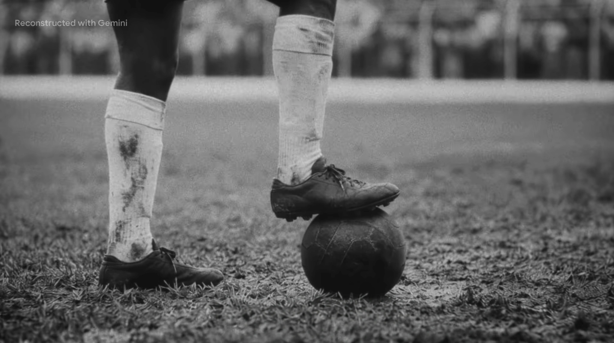Cena em preto e branco: chuteira apoiada sobre a bola no campo.