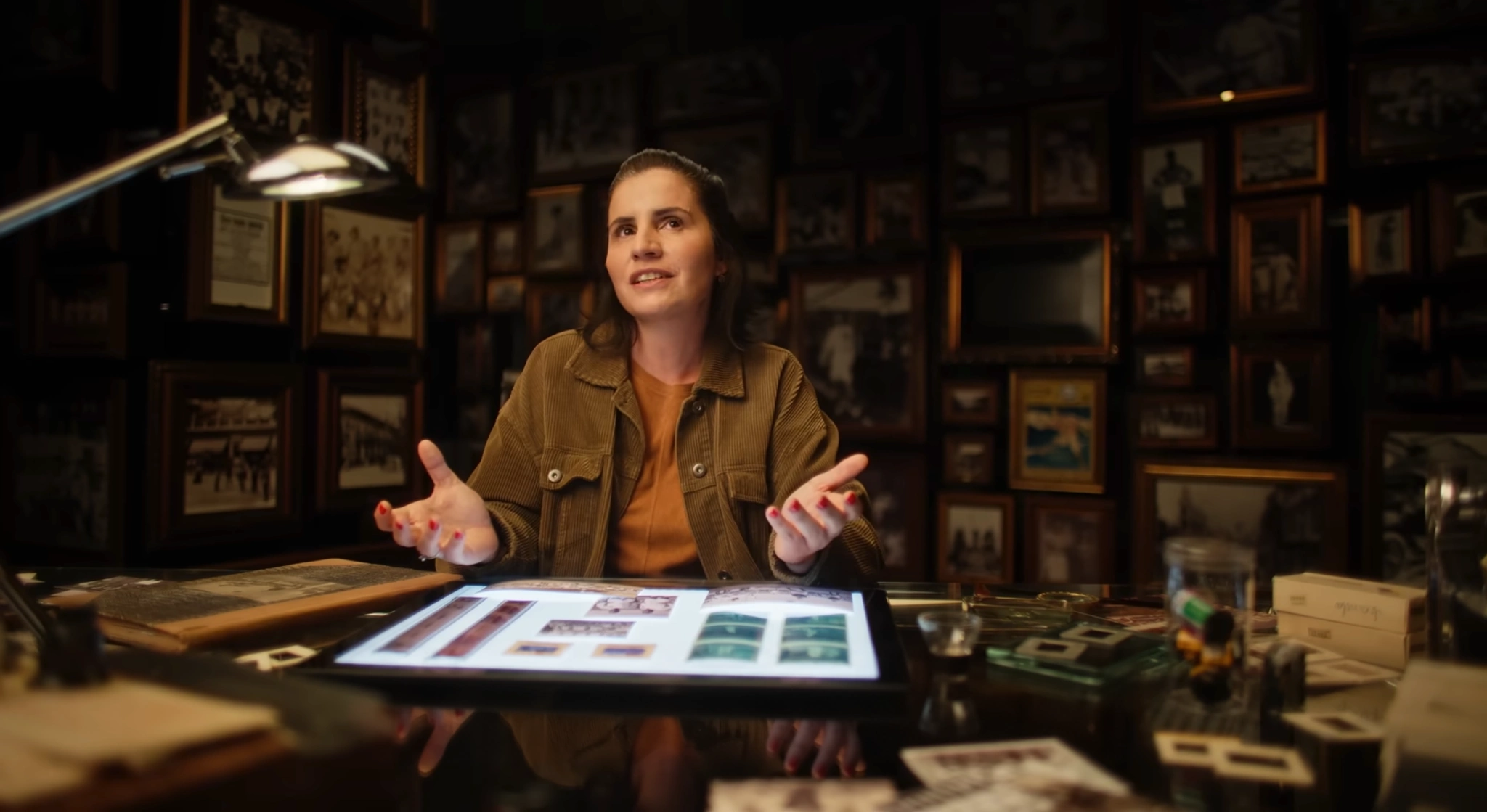 Mulher à mesa em uma sala com livros e fotografias.
