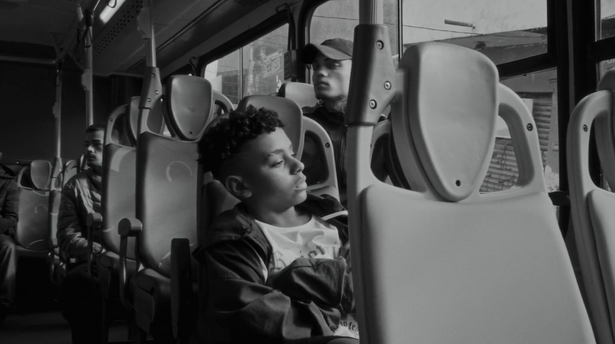 Menino com fones de ouvido sentado no ônibus, em preto e branco.