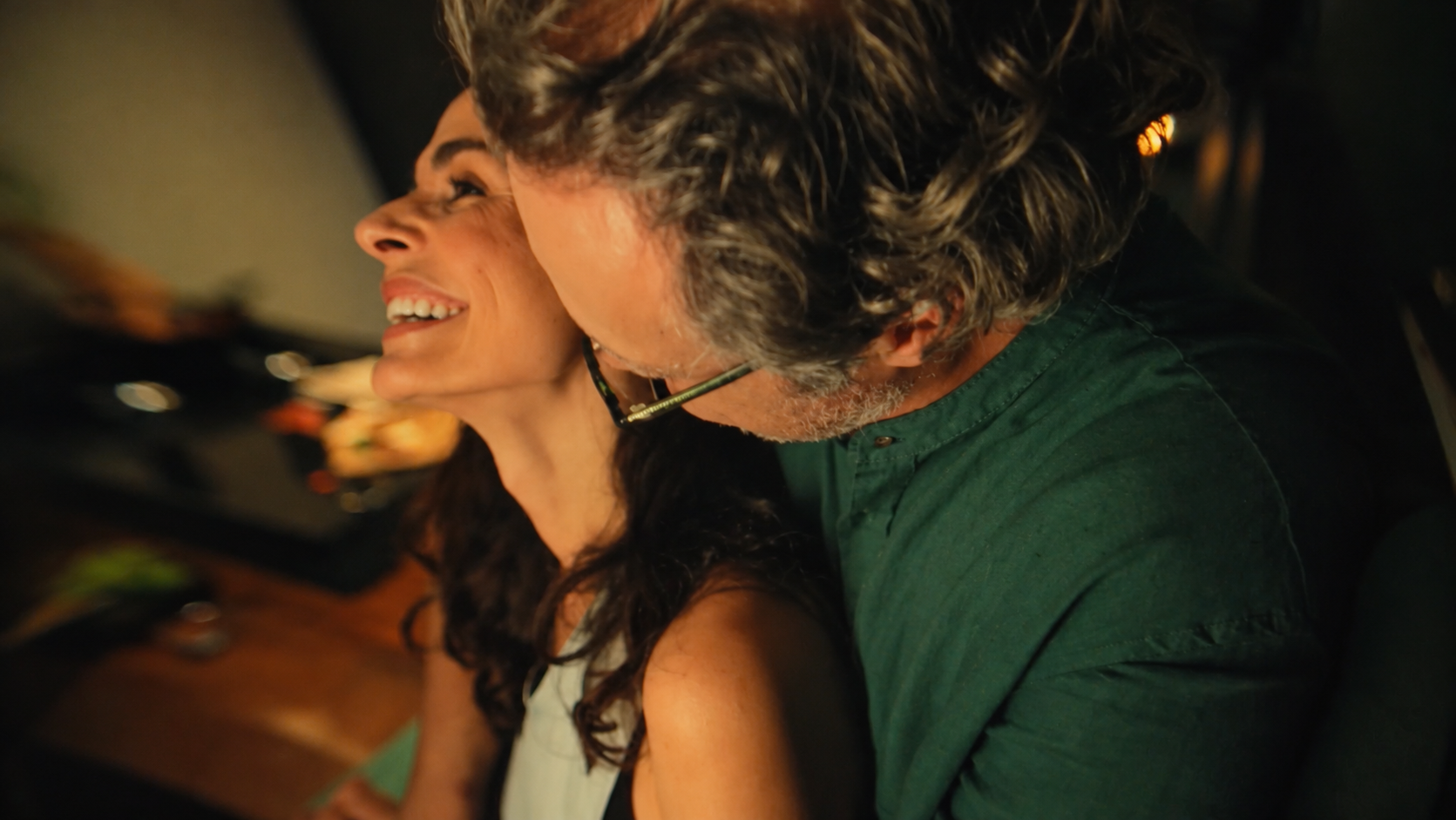 Casal se abraçando na cozinha, em um close com luz quente.