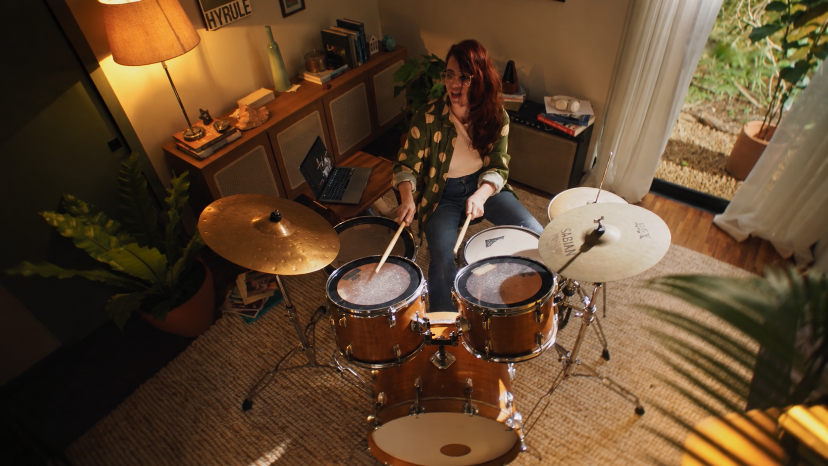 Vista de cima de uma baterista tocando em um quarto iluminado pela janela.