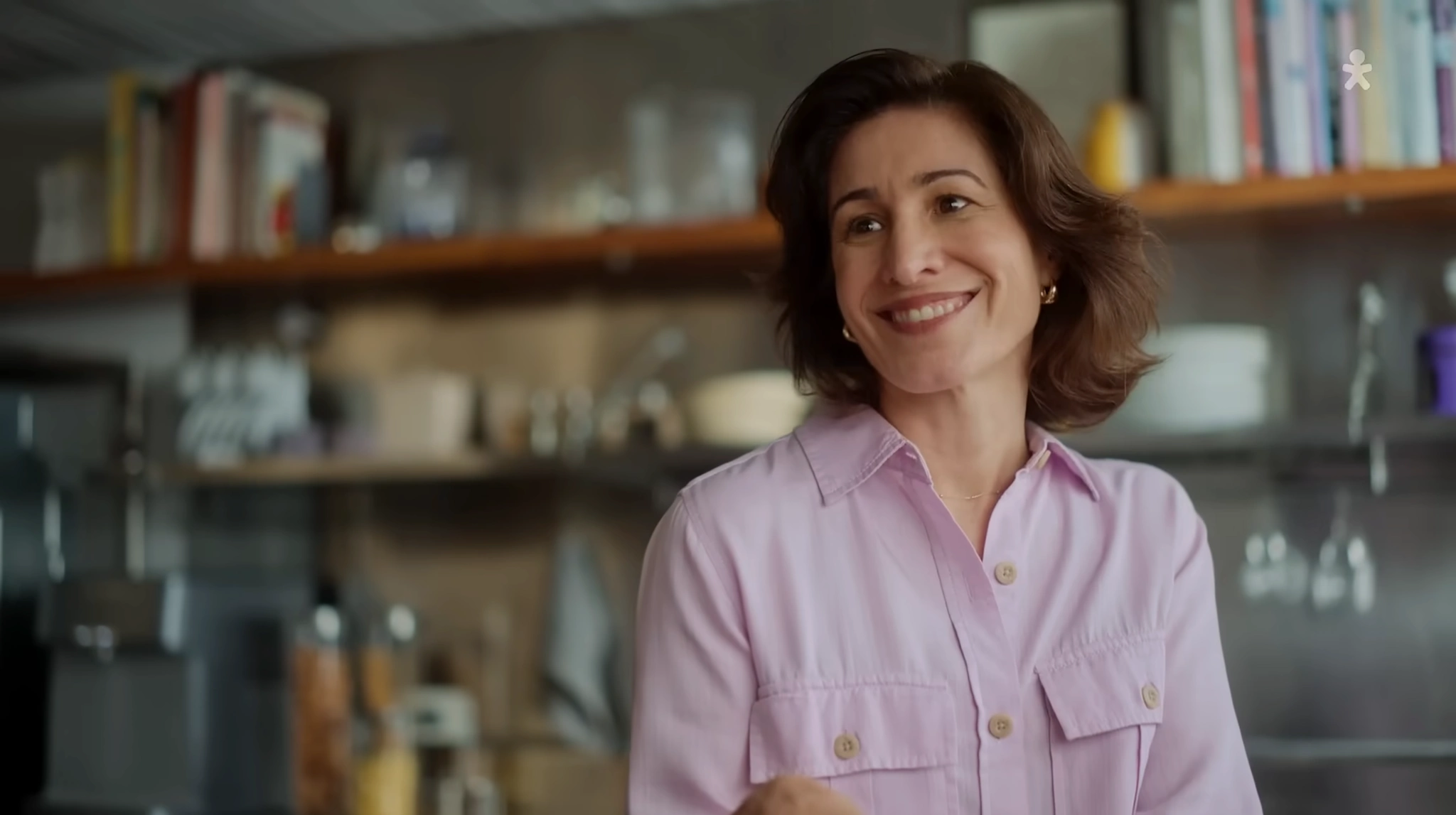 Mulher com camisa lilás diante de uma estante na cozinha.
