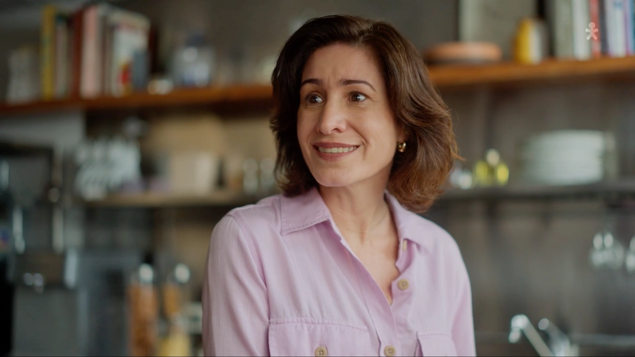 Mulher de camisa lilás sorrindo em frente à estante.